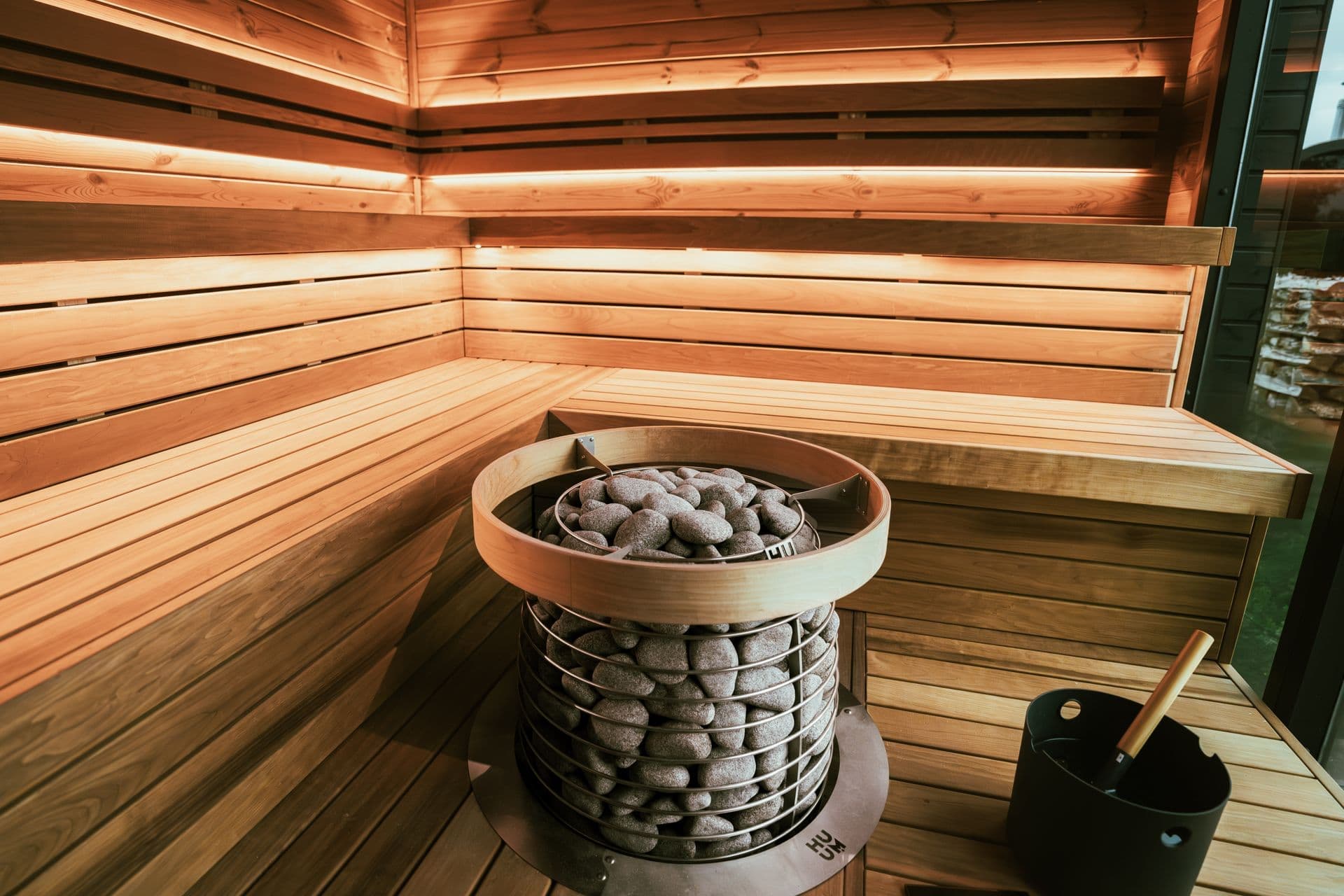 The cedar-lined interior of a home sauna, with a stone heater and a wooden bucket