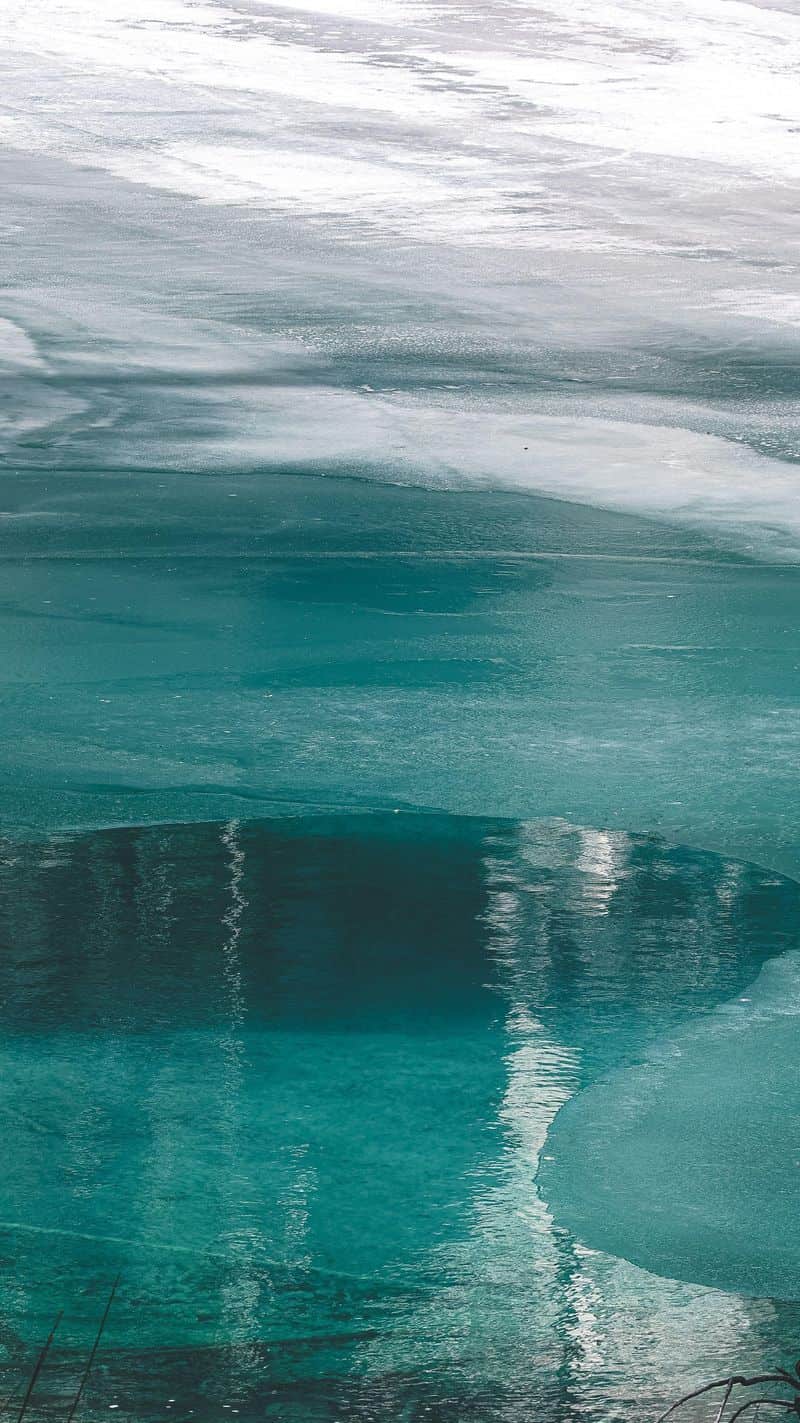Meltwater pooling over the teal ice of a frozen lake