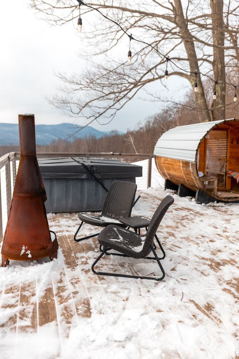 A barrel sauna on a snow-covered deck under winter mountains